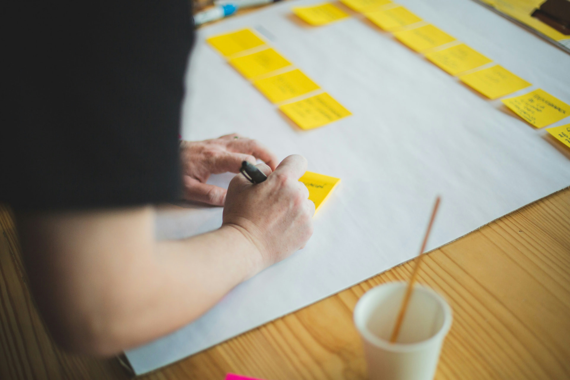 Hands writing on a yellow sticky note beside rows of notes laid out on paper